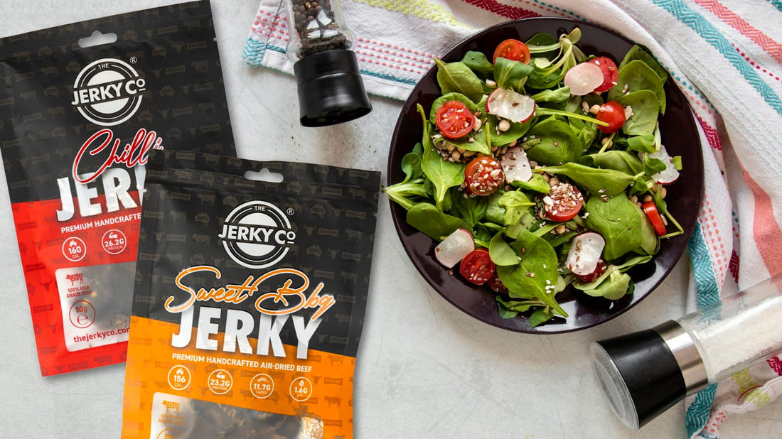 Beef jerky salad with leafy greens, cherry tomatoes and radish, with packets of The Jerky Co beef jerky on the side.