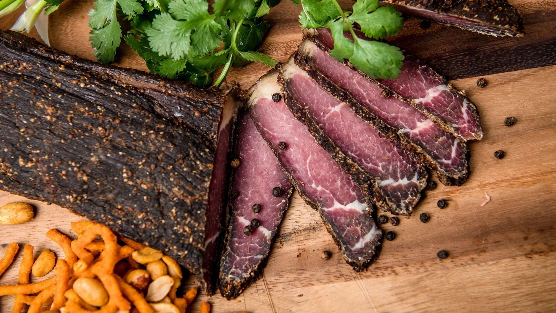 The Jerky Co traditional South African biltong made from premium air-dried Australian beef sliced on wooden board with spices and herbs.